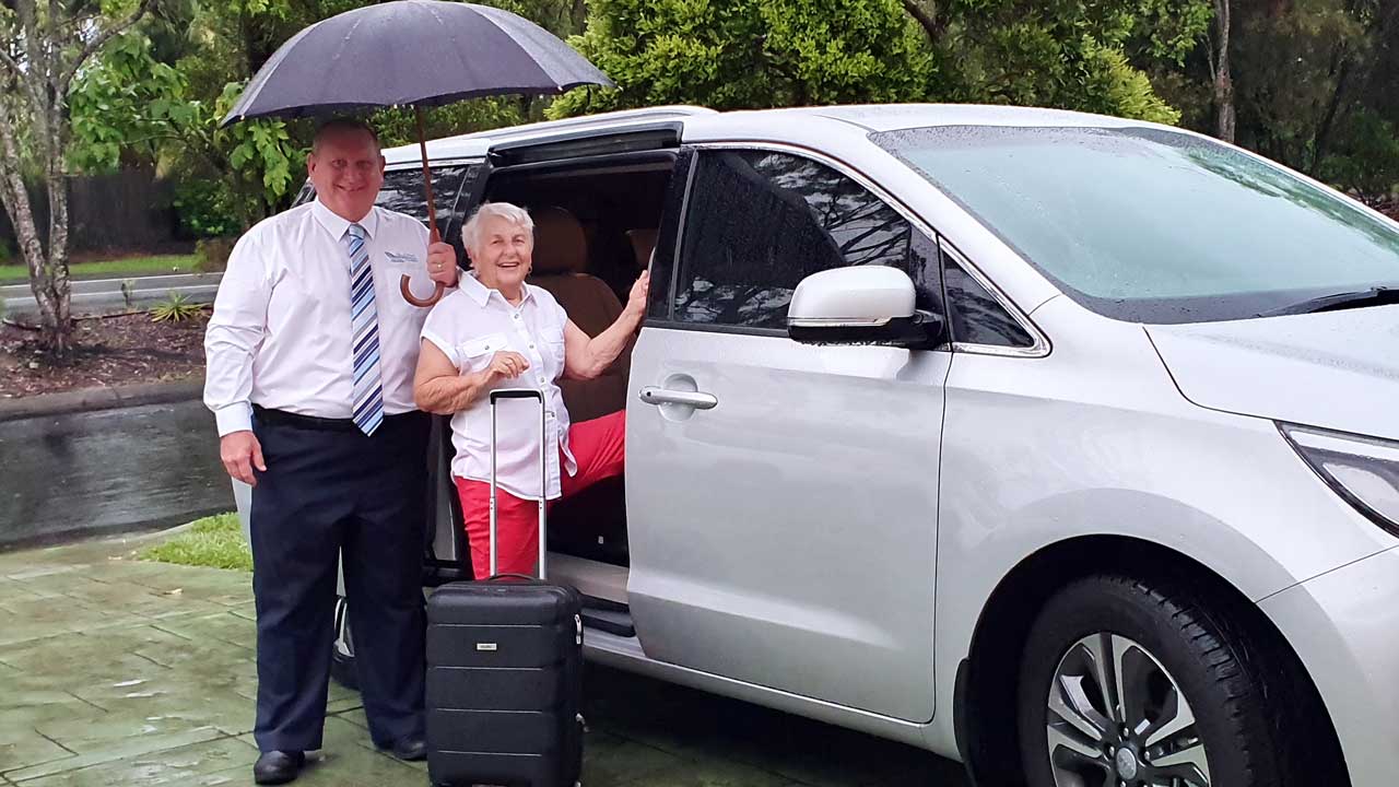 Private Transfers Sunshine Coast to Brisbane - elderly woman and driver holding an umbrella